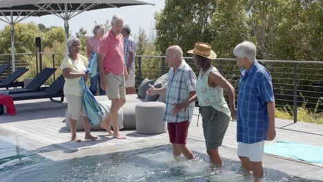 Happy-diverse-senior-friends-standing-in-pool-at-sunny-garden-party,-unaltered,-in-slow-motion