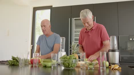 Happy-senior-caucasian-male-friends-preparing-health-drinks-in-kitchen,-unaltered,-in-slow-motion