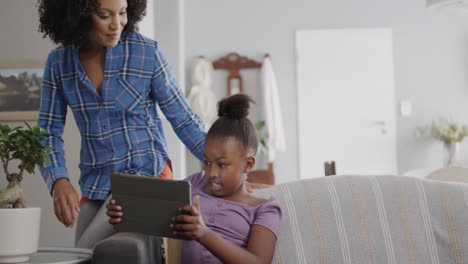 Glückliche-Afroamerikanische-Mutter-Und-Tochter-Sitzen-Auf-Dem-Sofa-Und-Benutzen-Ein-Tablet,-Zeitlupe,-Unverändert