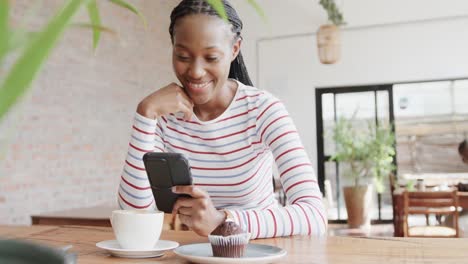 Feliz-Mujer-Afroamericana-Usando-Un-Teléfono-Inteligente-En-La-Mesa-En-Una-Cafetería,-Cámara-Lenta