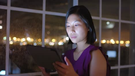 Reflexiva-Mujer-De-Negocios-Asiática-Usando-Tableta-Y-Mirando-Por-La-Ventana-De-La-Oficina-Por-La-Noche,-Cámara-Lenta