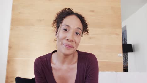 Happy-biracial-woman-making-video-call-talking-and-smiling-in-living-room,-in-slow-motion