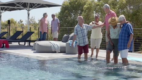 Happy-diverse-senior-friends-talking-and-splashing-in-pool-at-sunny-garden-party,-in-slow-motion