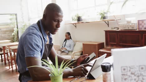 Vielbeschäftigter-Afroamerikanischer-Coffeeshop-Besitzer-Mit-Tablet-Und-Smartphone,-Zeitlupe