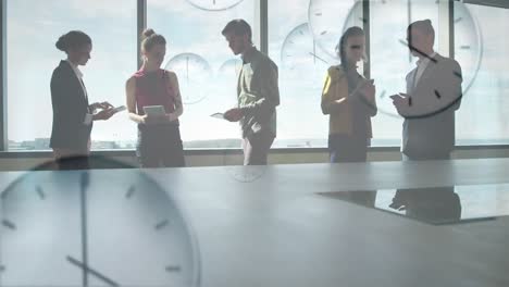 Animation-of-multiple-ticking-clocks-floating-against-diverse-businesspeople-working-at-office