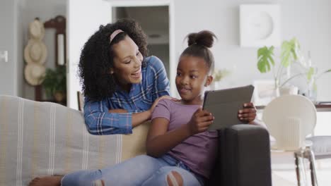 Glückliche-Afroamerikanische-Mutter-Und-Tochter-Sitzen-Auf-Dem-Sofa,-Benutzen-Tablet,-Zeitlupe