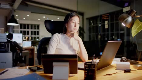 Focused-asian-casual-businesswoman-sitting-at-desk-using-laptop-in-office-at-night,-slow-motion