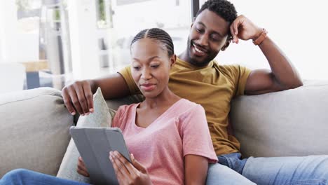 Happy-african-american-couple-using-tablet-and-talking-on-couch-at-home,-in-slow-motion