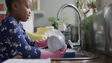 Happy-african-american-mother-and-daughter-washing-dishes-in-kitchen,-slow-motion
