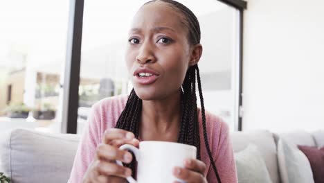 Portrait-of-happy-african-american-woman-with-coffee-making-video-call-and-laughing,-in-slow-motion