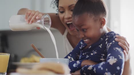 Happy-african-american-mother-and-daughter-eating-breakfast-in-kitchen,-slow-motion