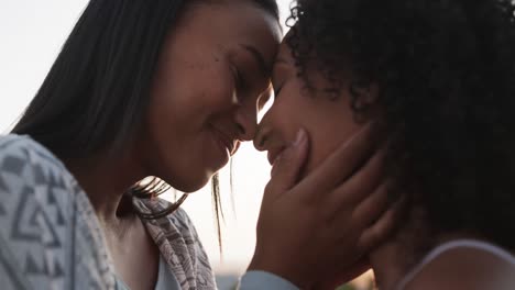Romantic-biracial-lesbian-couple-smiling-and-embracing-in-garden-at-sundown,-slow-motion