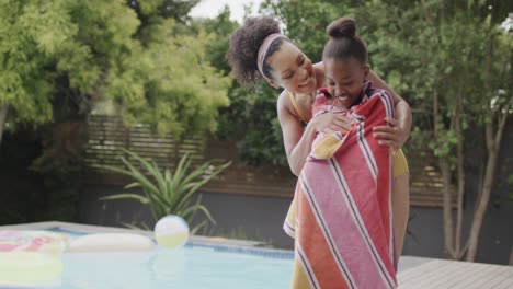 African-american-mother-and-daughter-covering-with-towel-by-swimming-pool-in-garden,-slow-motion