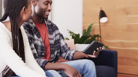 Glückliches-Afroamerikanisches-Paar,-Das-Auf-Der-Couch-Mit-Smartphone,-Tablet-Und-Laptop-In-Zeitlupe-Spricht