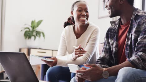 Glückliches-Afroamerikanisches-Paar,-Das-Taschenrechner-Und-Laptop-Benutzt-Und-Zu-Hause-über-Finanzen-Diskutiert,-Zeitlupe