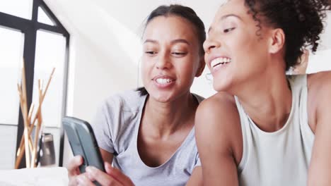 Happy-biracial-lesbian-couple-lying-on-bed-using-smartphone-together,-in-slow-motion