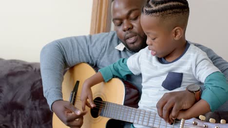 Glücklicher-Afroamerikanischer-Vater-Und-Sohn-Sitzen-Auf-Dem-Sofa-Und-Spielen-Gitarre,-In-Zeitlupe
