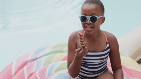 Portrait-of-happy-african-american-girl-smiling-and-eating-ice-cream-by-swimming-pool,-slow-motion