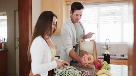 Happy-caucasian-couple-unpacking-grocery-shopping-together-in-kitchen,-slow-motion