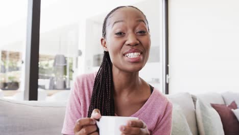 Portrait-of-happy-african-american-woman-with-coffee-making-video-call-and-waving,-in-slow-motion