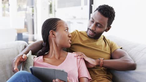 Glückliches-Afroamerikanisches-Paar,-Das-Tablet-Benutzt-Und-Zu-Hause-Auf-Der-Couch-Spricht,-In-Zeitlupe