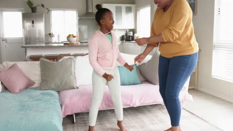 Happy-african-american-mother-and-daughter-having-fun-dancing-in-living-room,-in-slow-motion