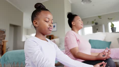 Happy-unaltered-african-american-mother-and-daughter-doing-yoga-meditation-at-home,-in-slow-motion