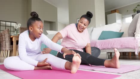 Happy-unaltered-african-american-mother-and-daughter-doing-yoga-stretching-at-home,-in-slow-motion
