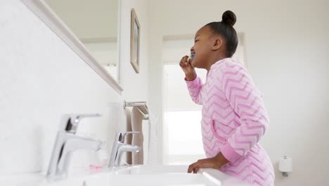 Happy-unaltered-african-american-girl-brushing-teeth-in-bathroom,-in-slow-motion