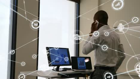 Animation-of-network-of-digital-icons-over-african-american-businessman-talking-on-smartphone