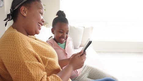 Happy-african-american-mother-and-daughter-sitting-on-sofa-using-tablet,-in-slow-motion