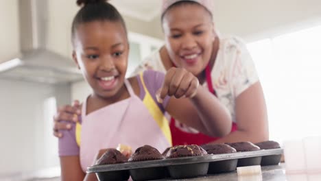 Happy-unaltered-african-american-mother-and-daughter-baking,-decorating-cupcakes,-in-slow-motion
