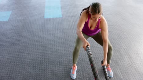 Focused-unaltered-biracial-woman-exercising-with-battling-ropes-at-gym,-in-slow-motion