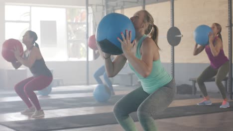 Focused-unaltered-diverse-women-lifting-medicine-balls-at-group-fitness-class-in-gym,-in-slow-motion