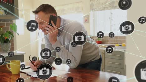 Animation-of-network-of-digital-icons-over-caucasian-man-talking-on-smartphone-at-home