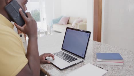 African-american-man-using-laptop-with-copy-space-on-screen-and-talking-on-smartphone,-slow-motion