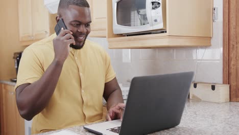 African-american-man-using-laptop-and-talking-on-smartphone,-in-slow-motion