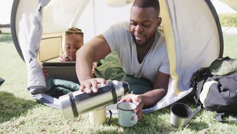 African-american-father-and-son-lying-in-tent-and-using-tablet-in-garden,-in-slow-motion
