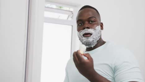 Hombre-Afroamericano-Aplicando-Crema-De-Afeitar-En-La-Cara-En-El-Baño,-En-Cámara-Lenta