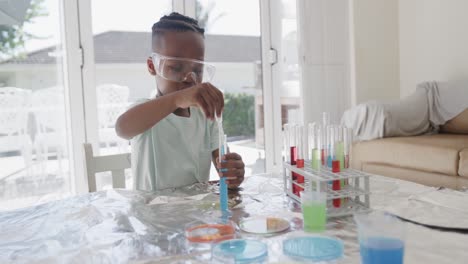 African-american-boy-sitting-at-table-holding-test-tubes-with-liquid,-in-slow-motion