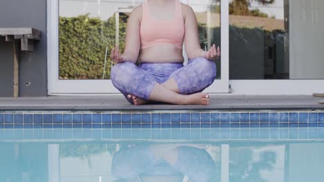 Konzentrierte-Gemischtrassige-Frau,-Die-In-Zeitlupe-Yoga-Praktiziert-Und-Am-Pool-Im-Garten-Meditiert
