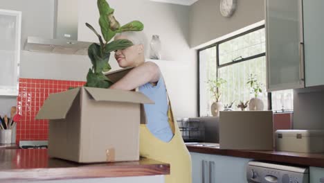 Happy-biracial-woman-unpacking-plant-from-carton-at-home-in-slow-motion