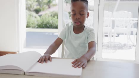 African-american-boy-sitting-at-table-and-reading-braille,-in-slow-motion