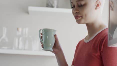 Happy-biracial-woman-drinking-coffee-at-home-in-slow-motion