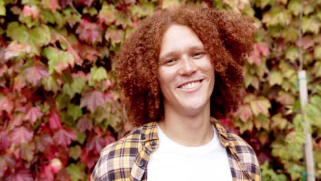 Portrait-of-happy-biracial-man-with-curly-red-hair-and-freckles-smiling-in-garden,-slow-motion