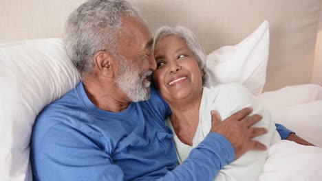 Glückliches-älteres-Gemischtrassiges-Paar,-Das-Auf-Dem-Bett-Liegt-Und-Sich-Unverändert-In-Zeitlupe-Umarmt
