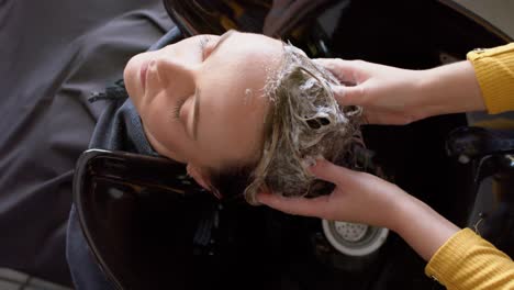 Hands-of-caucasian-female-hairdresser-washing-hair-of-relaxed-female-customer-at-hair-salon