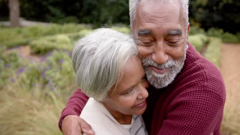Happy-senior-biracial-couple-embracing-and-smiling-in-garden,-unaltered,-in-slow-motion