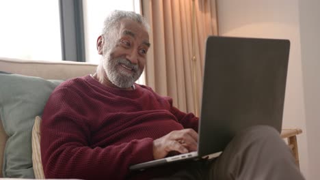 Happy-senior-biracial-man-using-laptop-for-video-call,-unaltered,-in-slow-motion