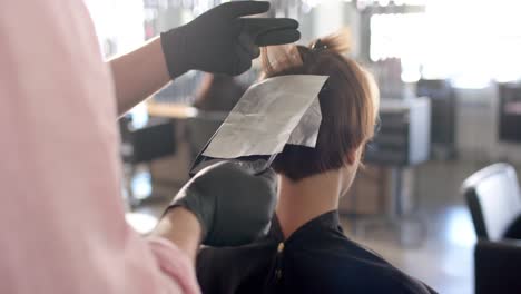 Hands-of-caucasian-male-hairdresser-highlighting-client's-hair-in-foil-at-salon,-in-slow-motion